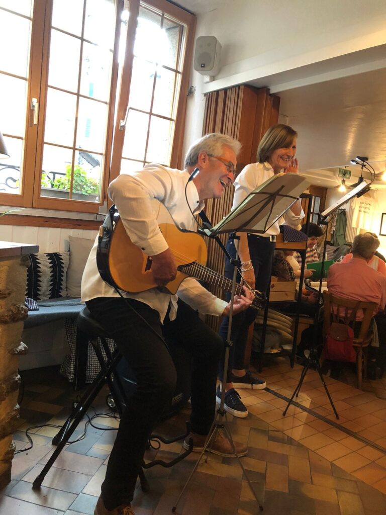 Café chantant dans le bar : un guitariste et une chanteuse près des fenêtres